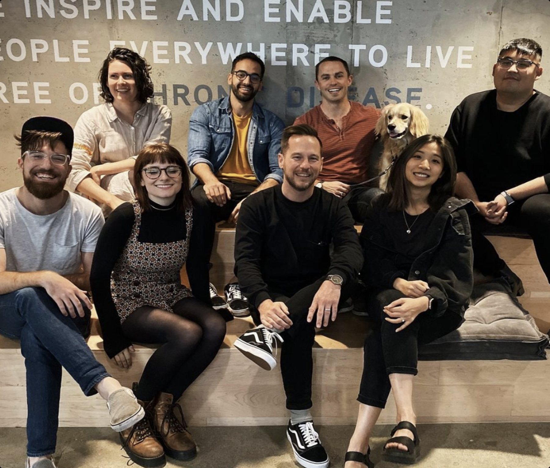 Design team at Omada sitting together in front of the mission wall